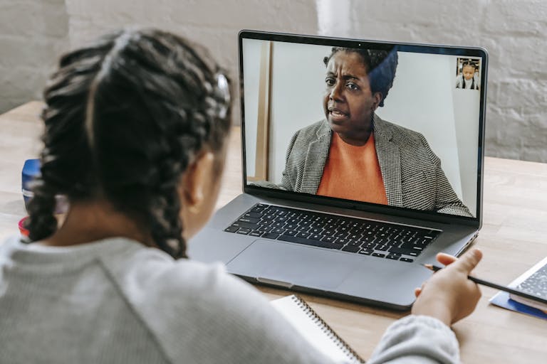 A child actively participates in a virtual learning session with a teacher via laptop.