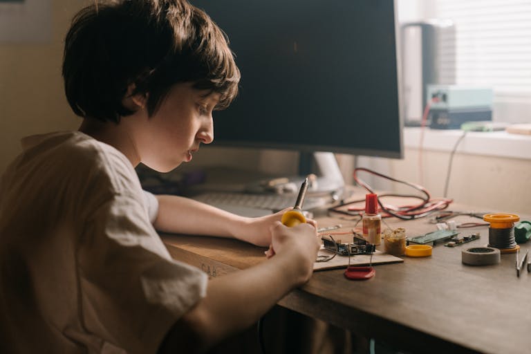 A young person soldering electronic components, showcasing DIY engineering and hobbyist skills indoors.