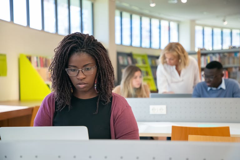 Diverse group of students collaborating in a contemporary library setting, focusing on studies with a mentor.