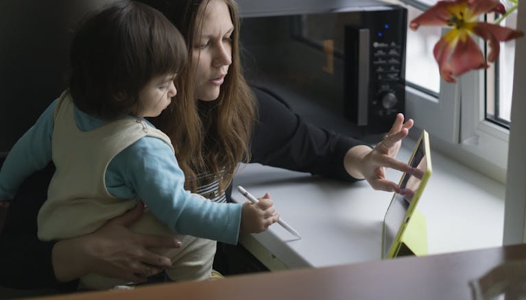 A mother and child interact with a tablet in the kitchen, fostering learning and bonding.