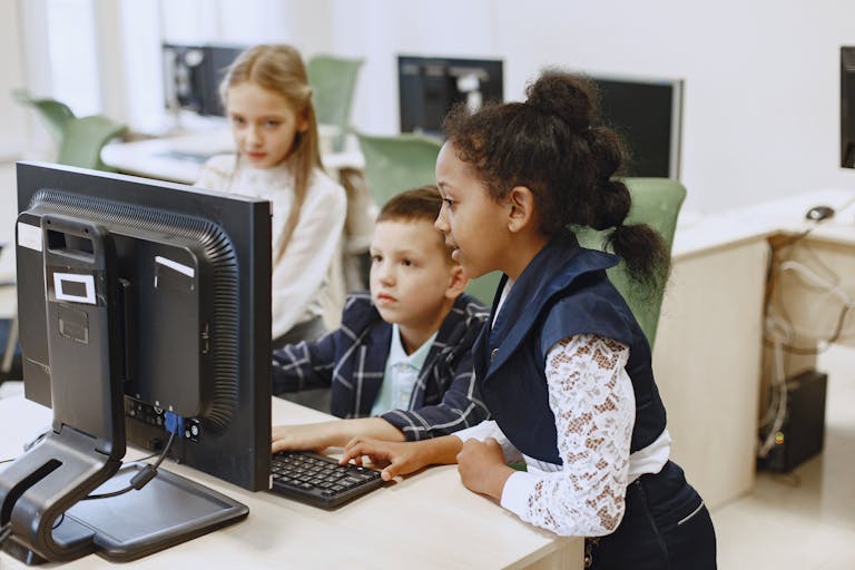 Diverse group of children working together on computers in a modern classroom setting.