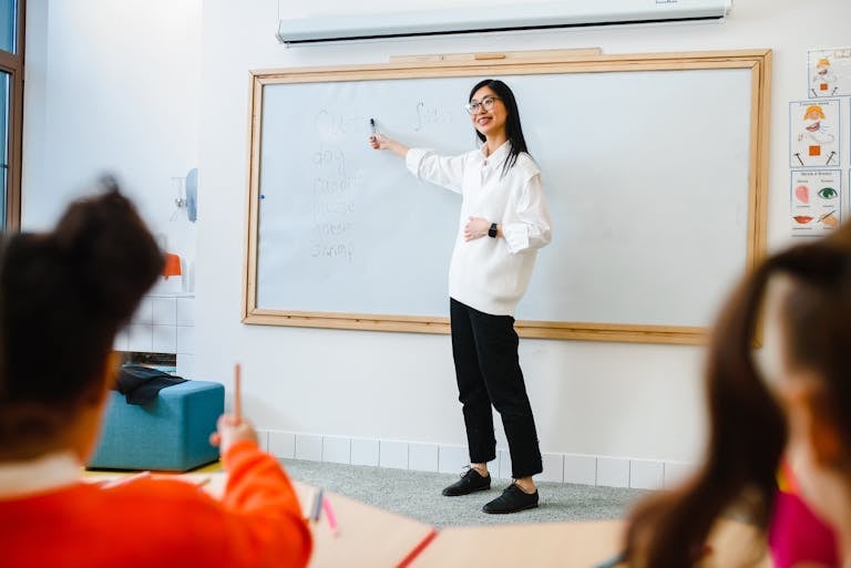 Smiling teacher instructing students in a classroom setting using a whiteboard.
