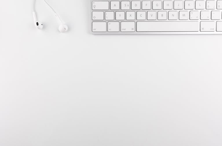 Top view of a white minimalist desk featuring a keyboard and earphones, ideal for technology themes.